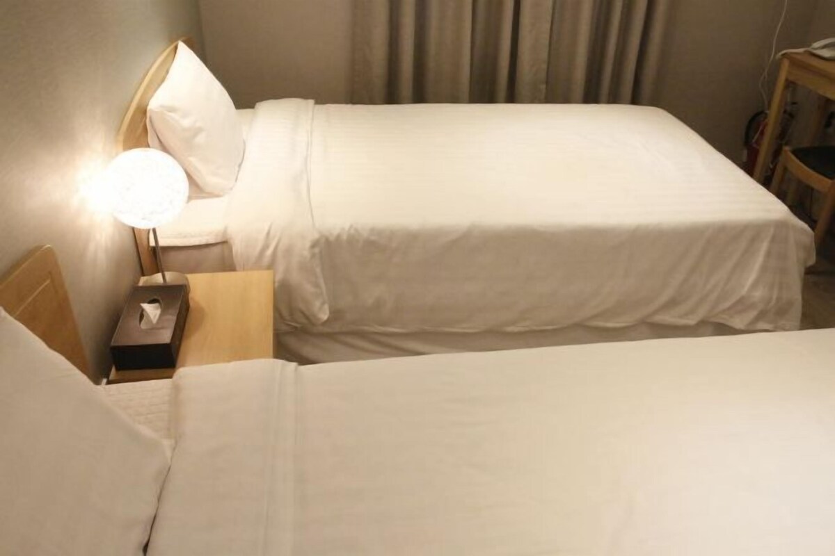 Ein Hotelzimmer mit zwei Betten, einem Nachttisch mit Lampe und einem weiteren Nachttisch mit Taschentuchbox.
