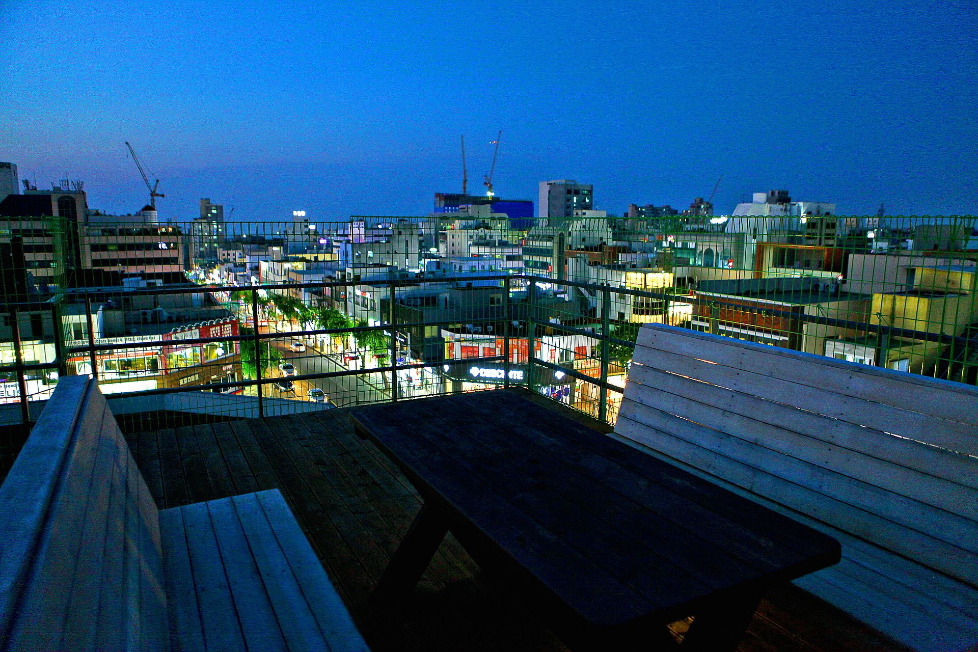 A view from a balcony with a wooden bench, overlooking a cityscape at dusk.