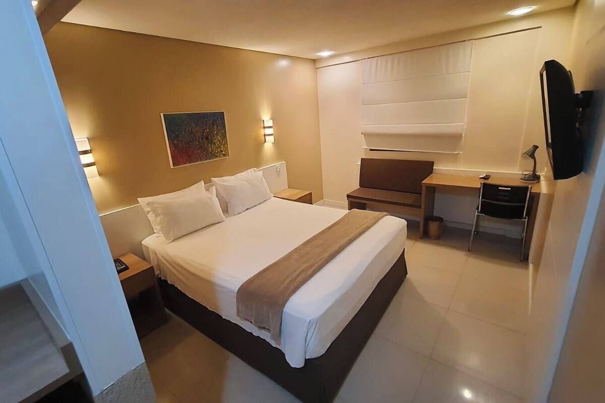 A modern hotel room with a large bed, bedside tables, a desk, and a TV.