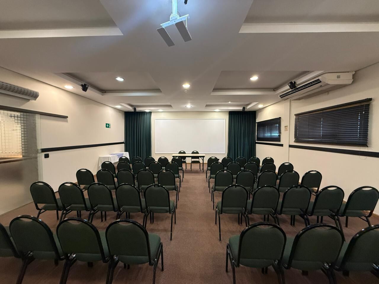 A conference room with rows of chairs, a projector screen, and a presentation table.