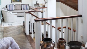 Un loft spacieux avec de hauts plafonds, des fenêtres de toit, un escalier et une décoration rustique comprenant des casseroles en cuivre et un tapis à motifs.