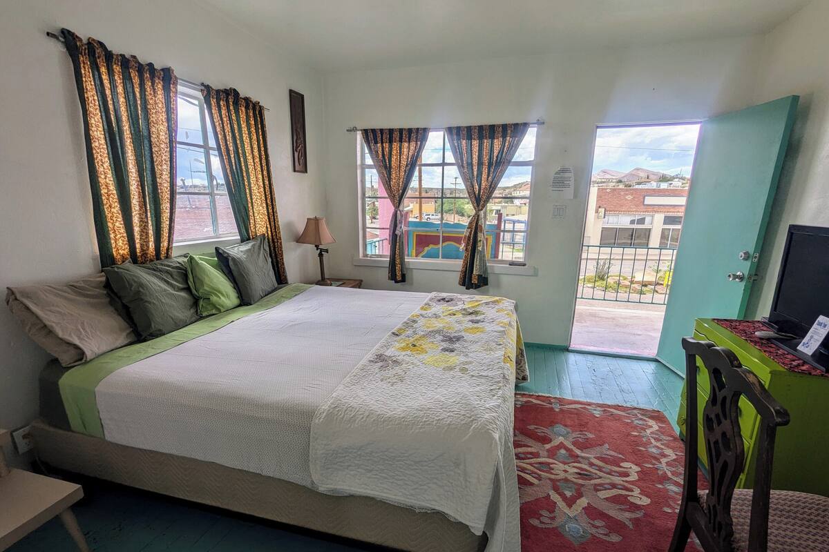 A bedroom with a bed, curtains, a lamp, a TV, and a view of the outside.