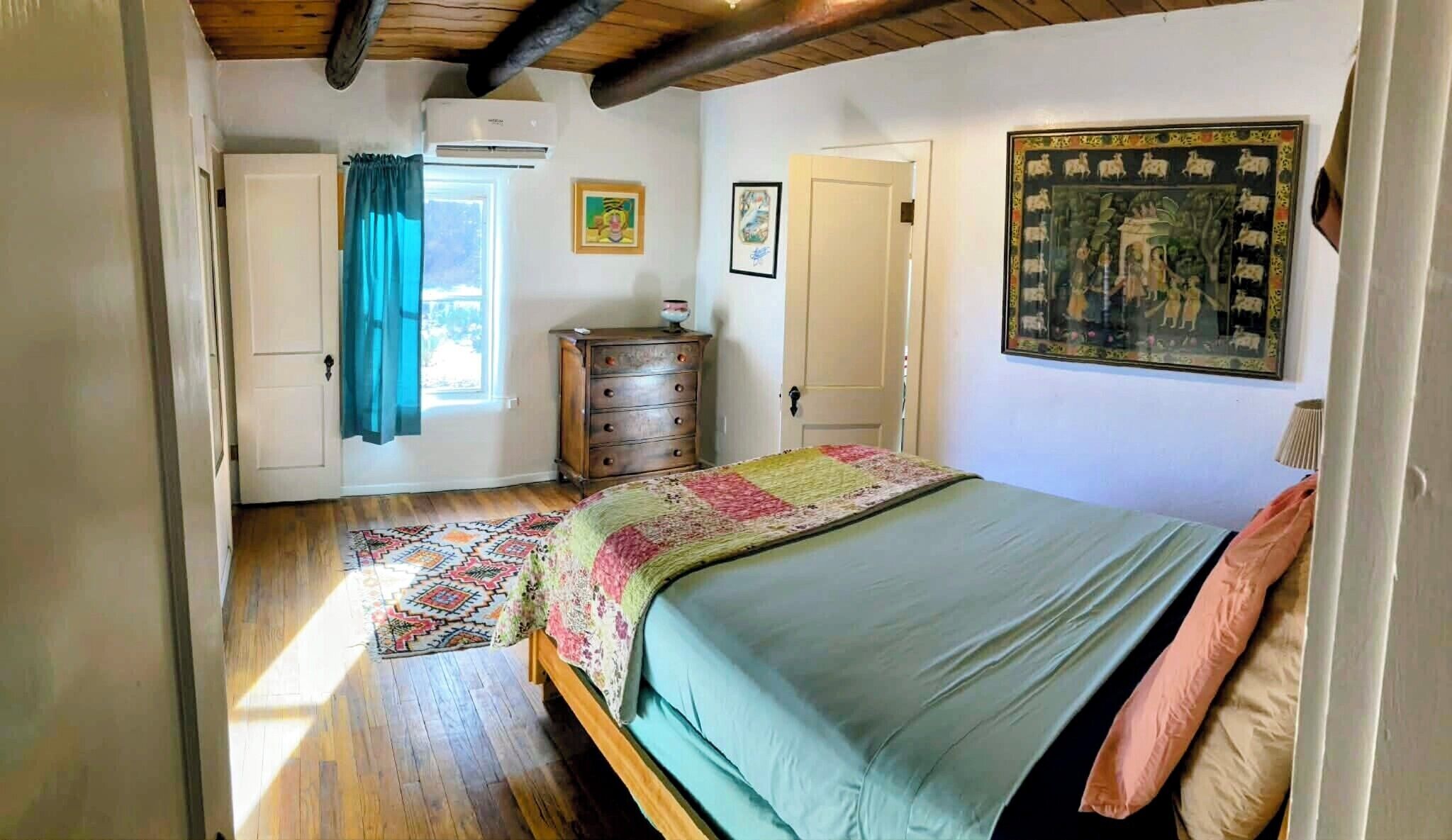 A bedroom with a bed, a dresser, a window with curtains, and a painting on the wall.