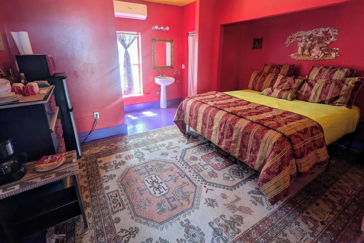 A bedroom with a bed, a bedside table, a mirror, and a window.