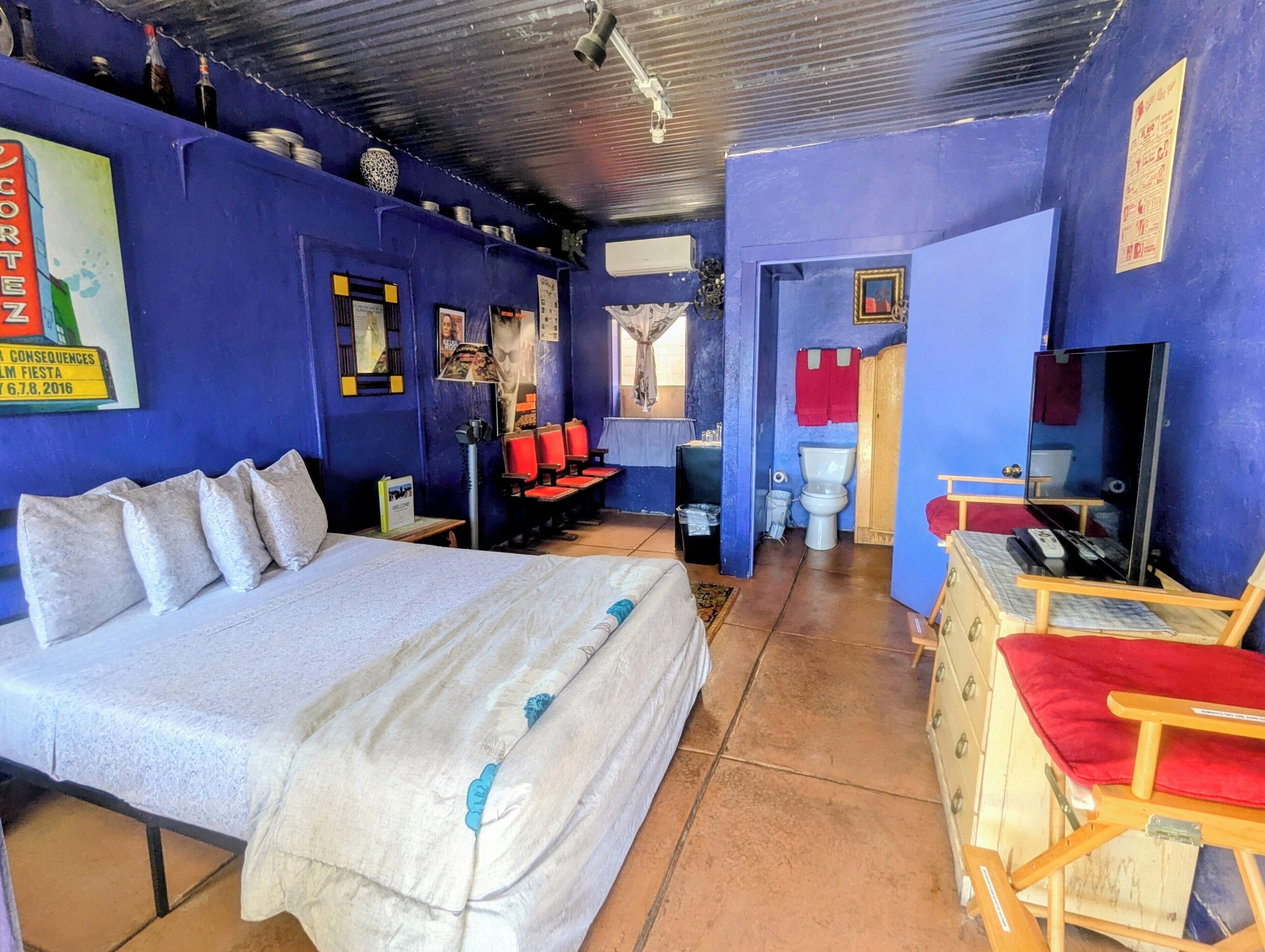 Una habitación con cama, escritorio, silla, inodoro y espejo.