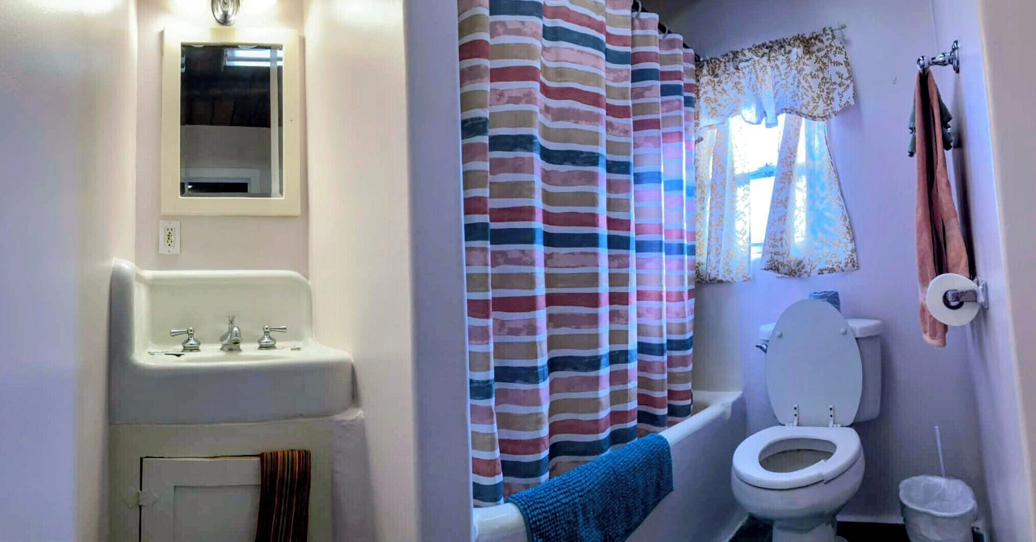 A bathroom with a white sink, a toilet, a striped shower curtain, and a towel hanging on the wall.