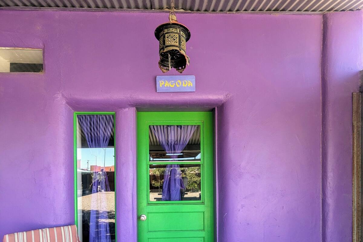 A purple building with a green door, a sign reading "PAGODA", a window with curtains, and a striped chair outside.