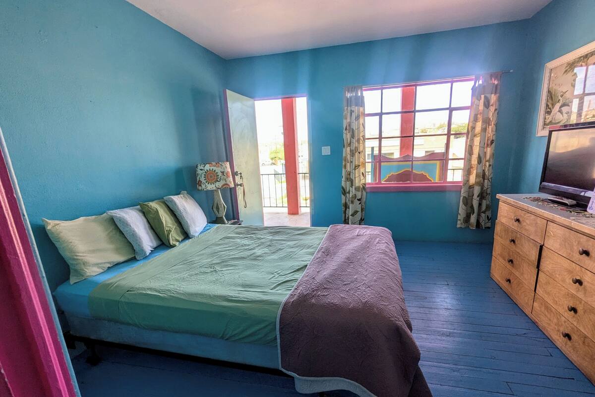 A bedroom with a bed, a wooden dresser, a television, and a window with curtains.