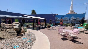 An outdoor patio area with tables and chairs, a rock garden, and a mural on the building.
