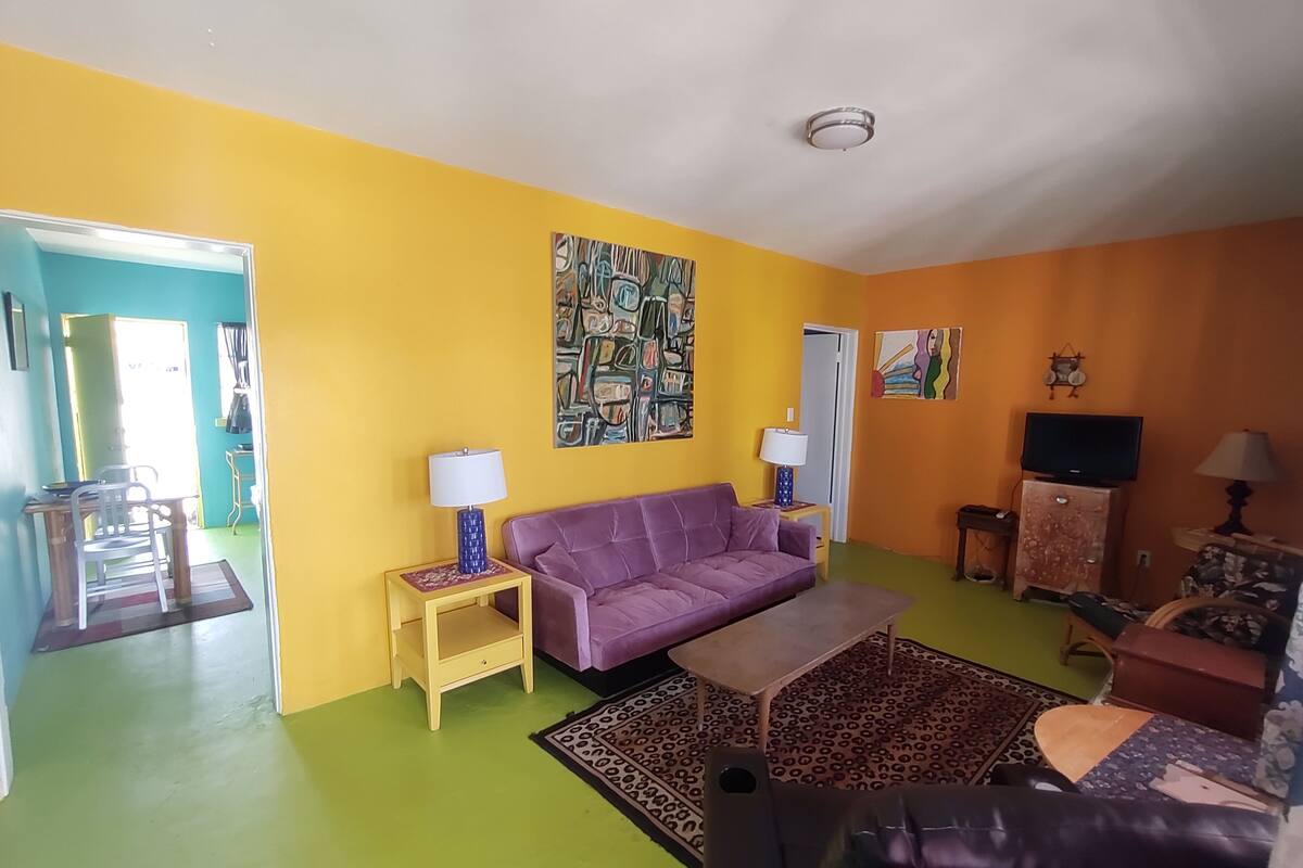 A living room with a purple sofa, a coffee table, and a leopard print rug. There are two lamps on side tables, a TV on a cabinet, and a painting on the wall.