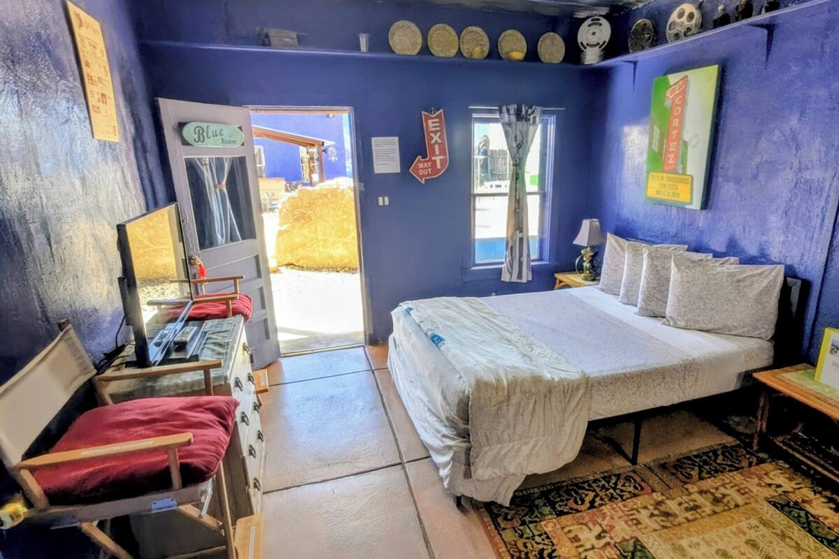 A room with a bed, a desk, a chair, a window, and a door leading outside.