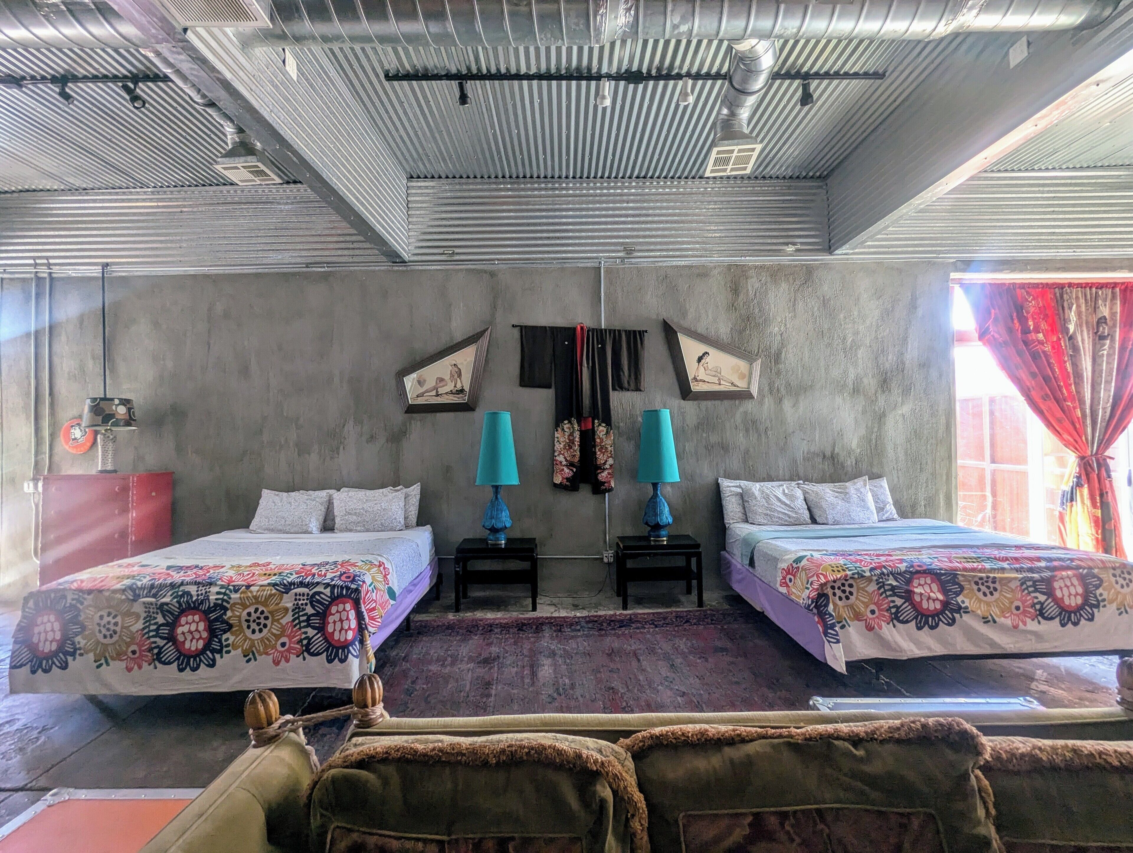 Um quarto com duas camas, um armário vermelho, um tapete estampado e uma janela com cortinas vermelhas.