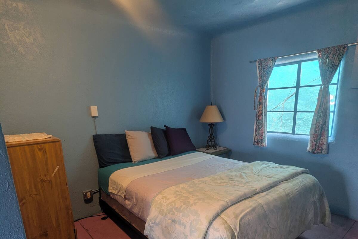 A bedroom with a bed, a nightstand, a lamp, and a window with curtains.
