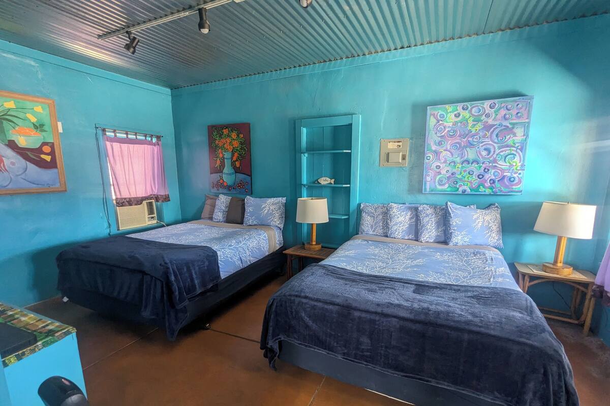 A room with two beds, a shelf with decorative items, and a wall with colorful artwork.