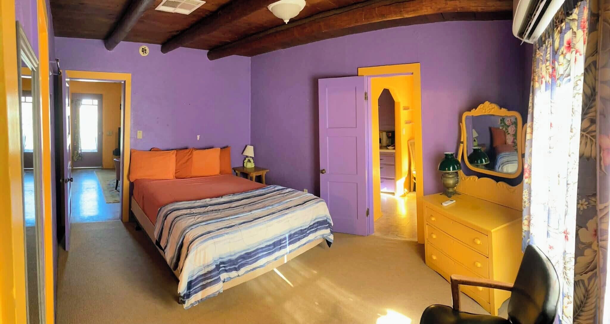 A bedroom with a bed, a dresser, a mirror, and a door leading to another room.