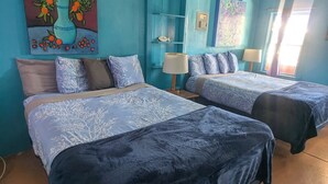 A room with two beds, a blue wall, a painting of flowers, and a shelf with a fish.