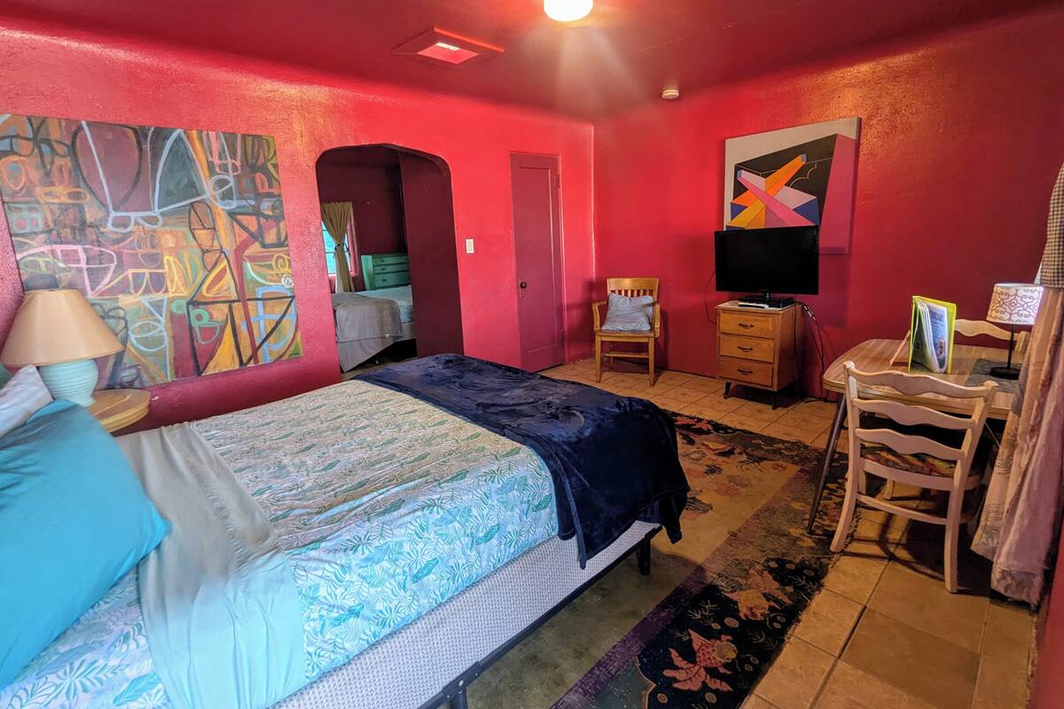 A room with a bed, a chair, a TV, and a desk.