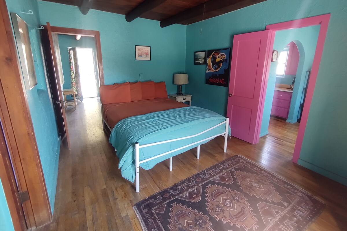 A bedroom with a bed, a nightstand, a lamp, and a door leading to another room.