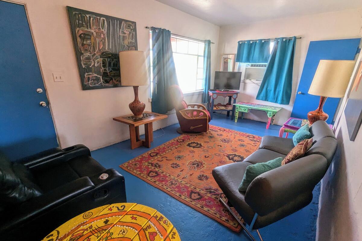 A living room with a sofa, a small table, a lamp, a rug, and a wall painting.