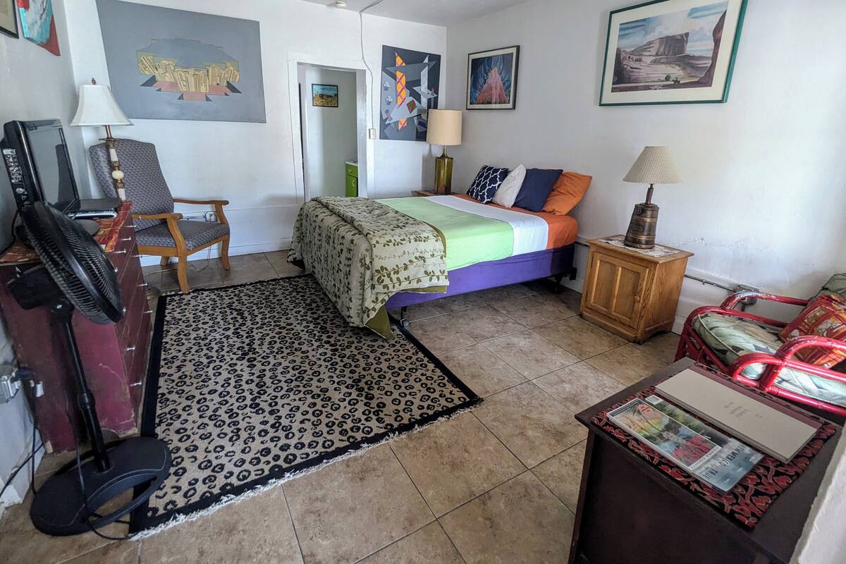 A bedroom with a bed, two chairs, a desk with a computer, and a lamp.