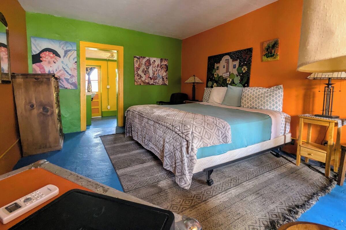 A room with a bed, a desk, a lamp, and a door leading to another room.