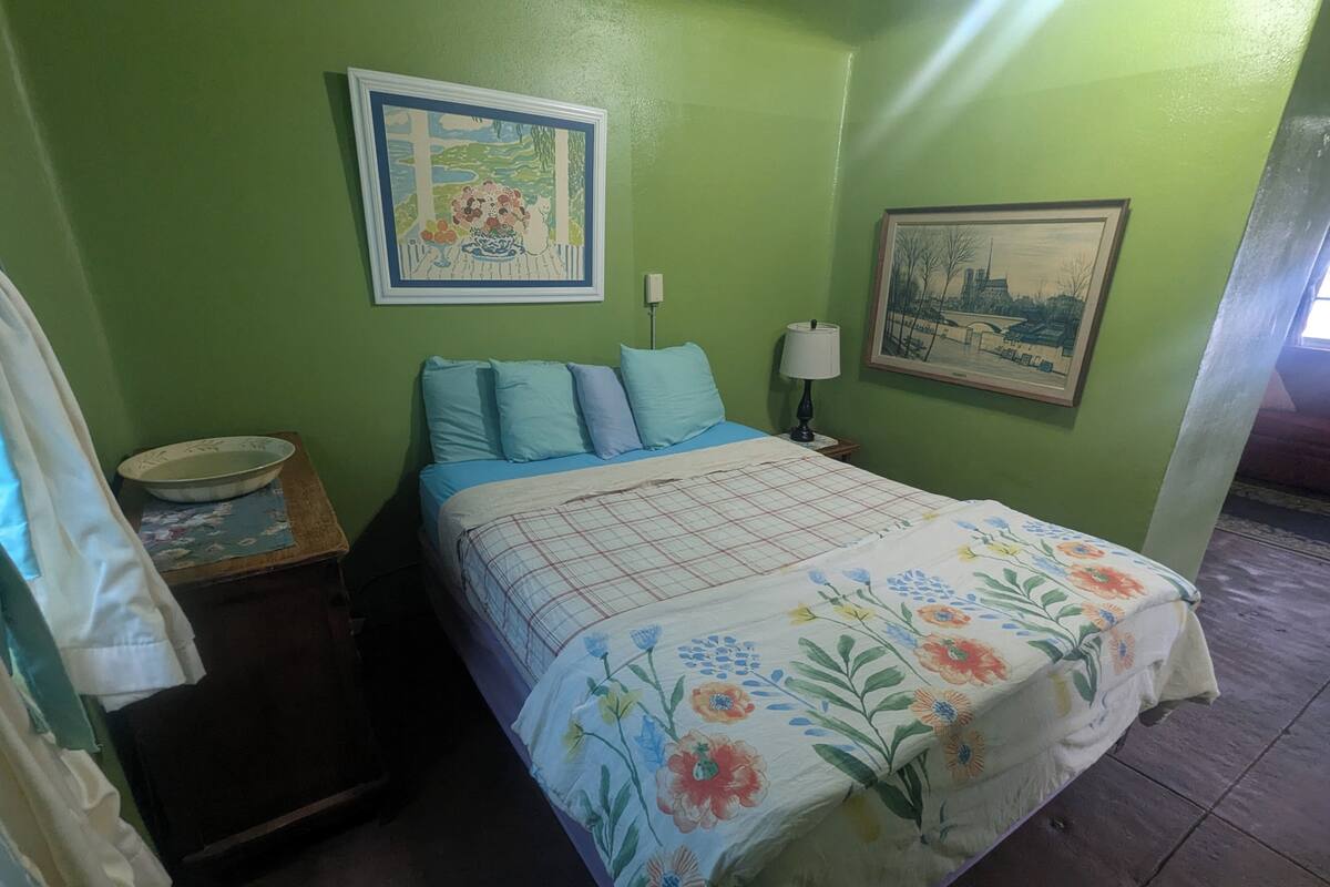 A bedroom with a bed, pillows, a nightstand, a lamp, and two framed pictures on the wall.