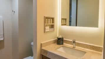Une salle de bain moderne avec des toilettes blanches, un grand miroir et un comptoir de couleur beige.