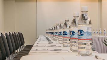 Un salón de conferencias con filas de sillas, botellas de agua y bolígrafos sobre una mesa.