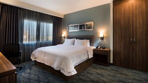A hotel room with a large bed, a desk, a chair, a nightstand, and a wardrobe. - Hampton Inn & Suites by Hilton Salamanca Bajio (Salamanca)