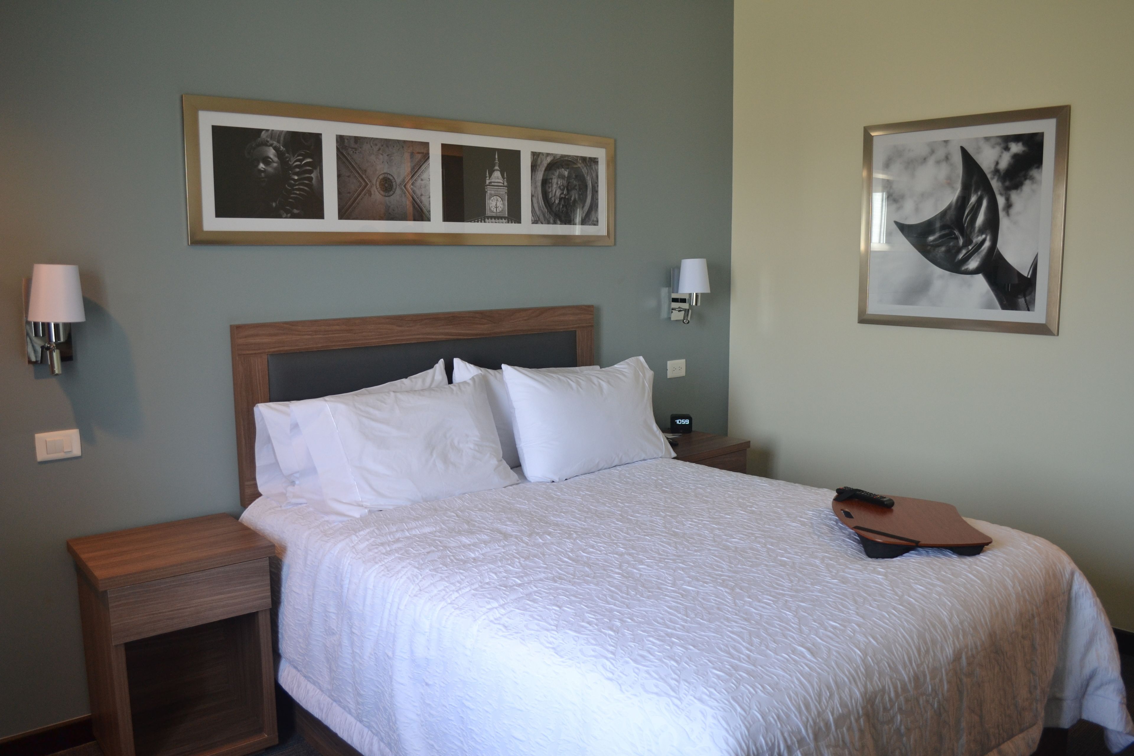 A neatly made bed with white linens, a wooden headboard, and a framed picture above it.
