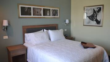 A neatly made bed with white linens, a wooden headboard, and a framed picture above it.