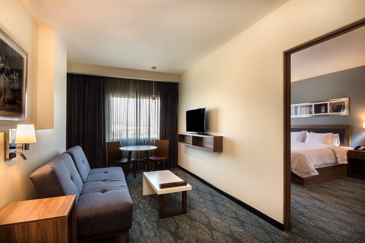 A hotel room with a sofa, a small table, a TV, a bed, and a dining area with chairs.