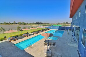 A pool area with multiple swimming pools, lounge chairs, umbrellas, and a building with large windows. - Hampton Inn & Suites by Hilton Salamanca Bajio (Salamanca)