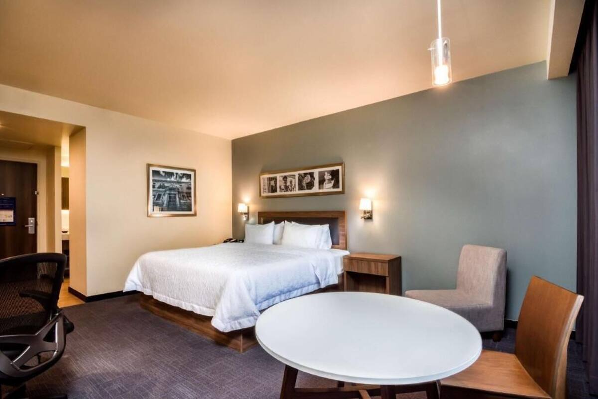 A hotel room with a bed, a round table, two chairs, a nightstand, and wall-mounted lights.
