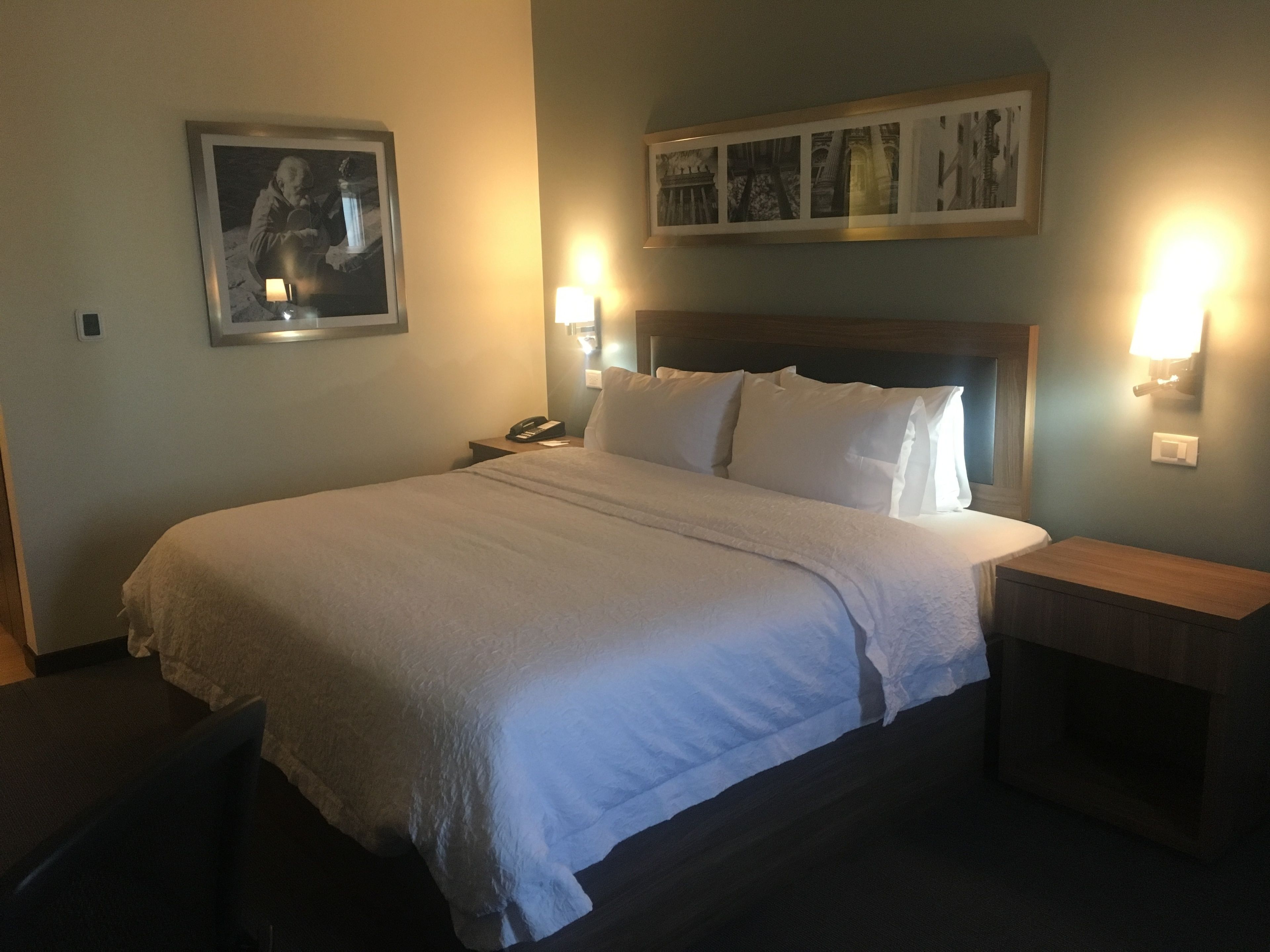 A hotel room with a large bed, a nightstand with a phone, and wall-mounted lamps.