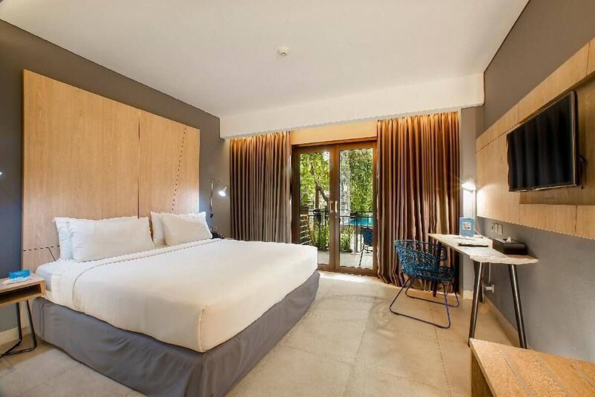 A modern hotel room with a large bed, a desk, a chair, and a TV.
