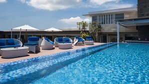 A pool area with lounge chairs and umbrellas, a modern building in the background, and a clear blue sky. - Solia Legian Bali (Legian)