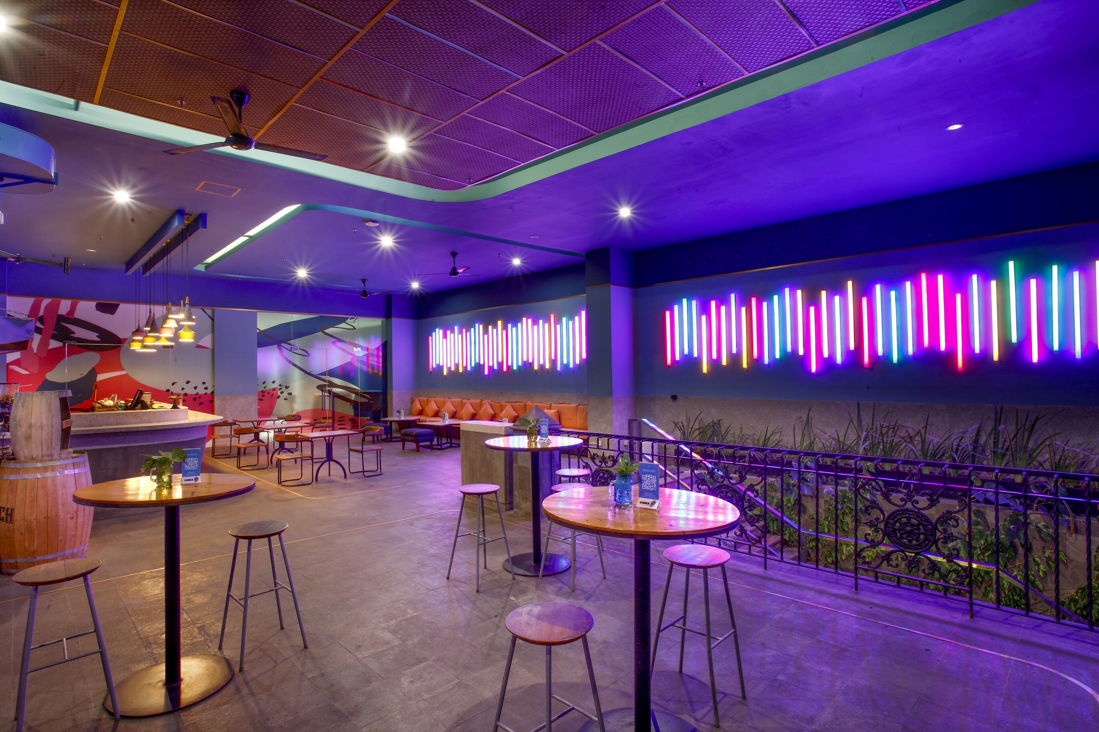 A modern interior with round tables and stools, a bar area, and a neon light display on the wall.