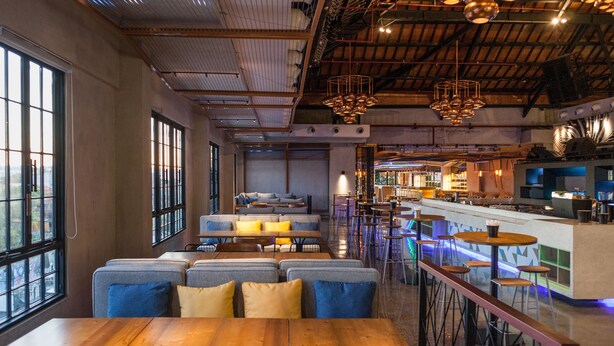 A modern restaurant with high ceilings, exposed beams, and a mix of seating including booths and bar stools. - Solia Legian Bali (Legian)