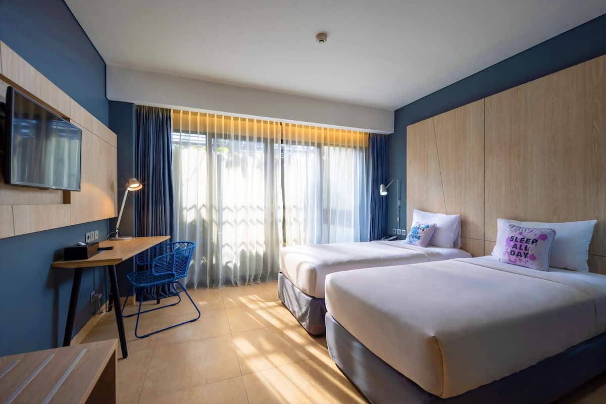 A hotel room with two beds, a desk, a chair, and a TV.