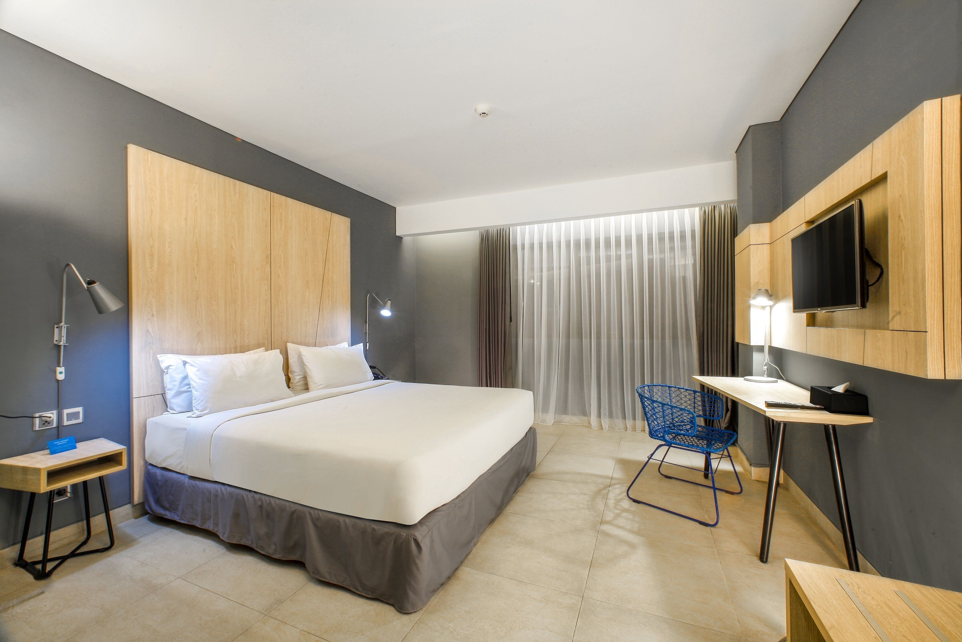 Una habitación de hotel moderna con cama, escritorio, silla, televisor y ventana con cortinas.