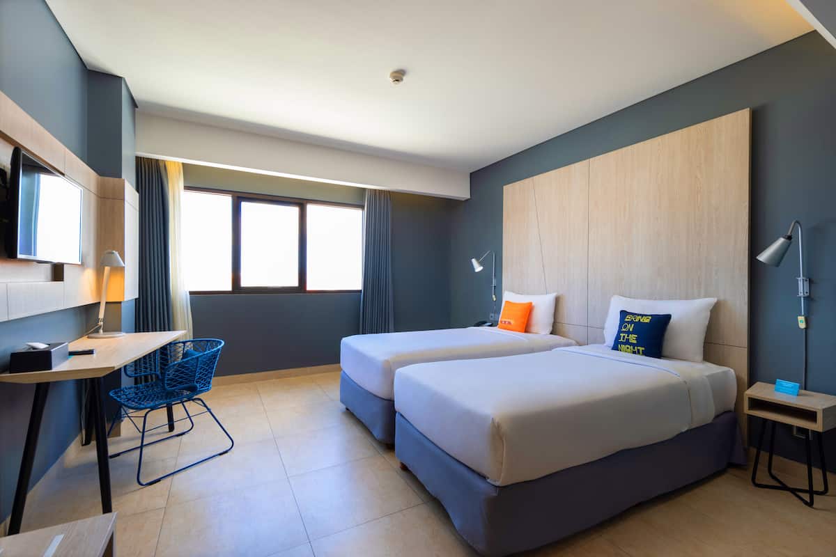 A hotel room with two beds, a desk, a chair, and a large window.