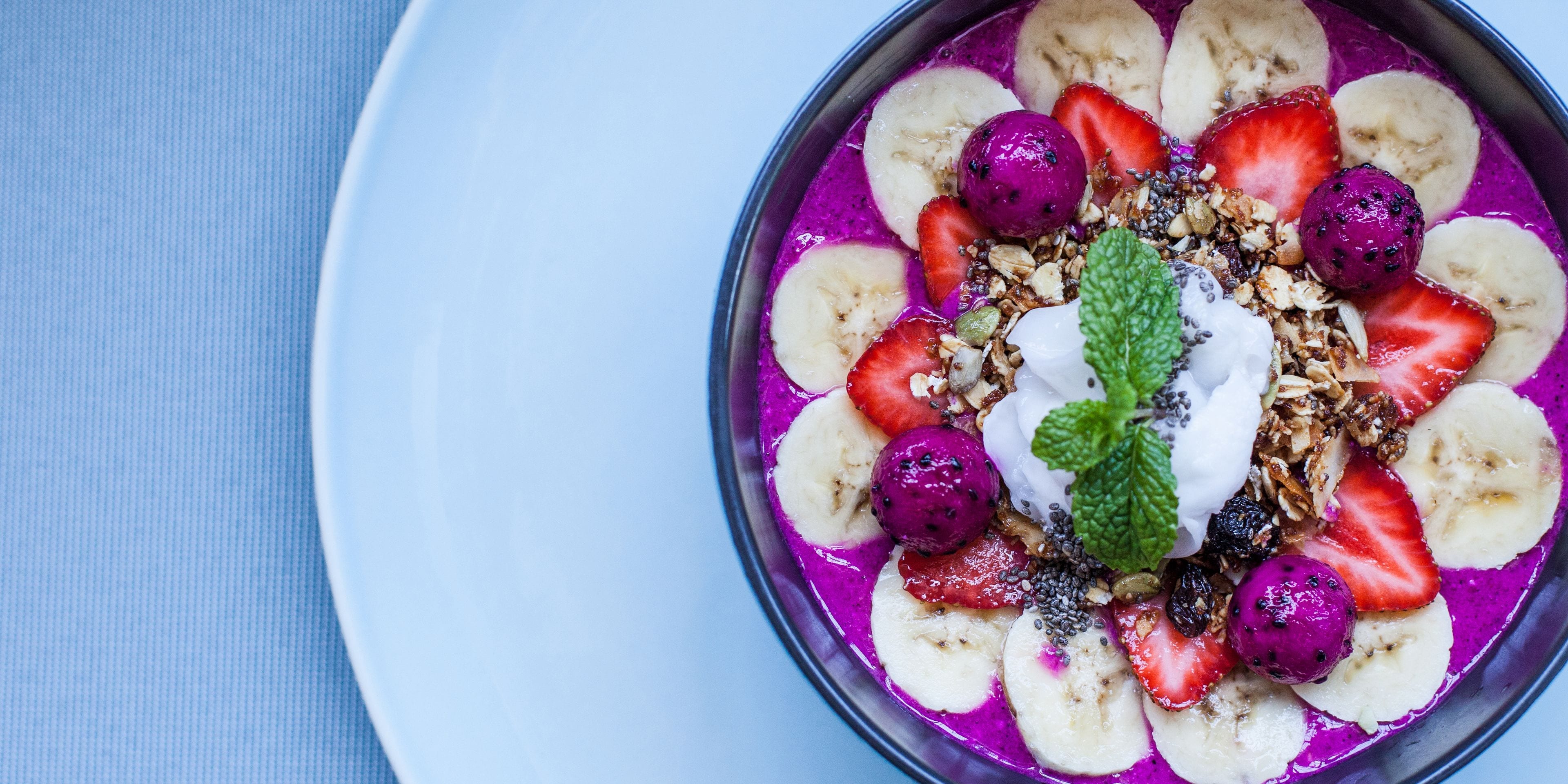 A bowl of colorful fruit and granola with a dollop of yogurt and a mint leaf on top.
