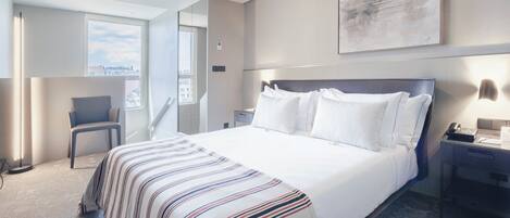 A hotel room with a large bed, a desk, a chair, and a city view.