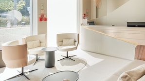 Een moderne hotellobby met een receptiebalie, een zithoek met banken en tafels, en grote ramen met uitzicht op het omliggende landschap.