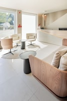 A modern hotel lobby with a reception desk, seating area with sofas and tables, and large windows offering a view of the outdoors.