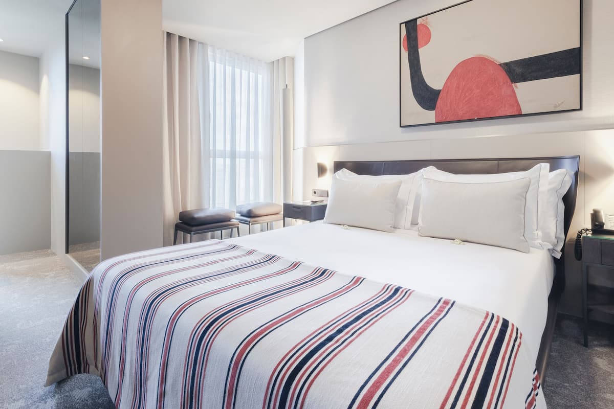 Een hotelkamer met een groot bed, een bureau, een stoel, een raam met gordijnen en een schilderij aan de muur.