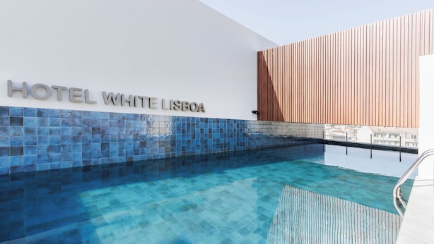 Een modern hotel met een helder zwembadgedeelte, een bord met de tekst 'HOTEL WHITE LISBOA' en een wand van houten latten.