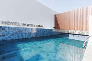 Un hôtel moderne doté d’un espace piscine bien aménagé, d’une enseigne indiquant « HÔTEL WHITE LISBOA » et d’un mur décoré de lattes de bois.
