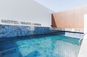A modern hotel with a clear pool area, a sign reading "HOTEL WHITE LISBOA", and a wooden slatted wall design.